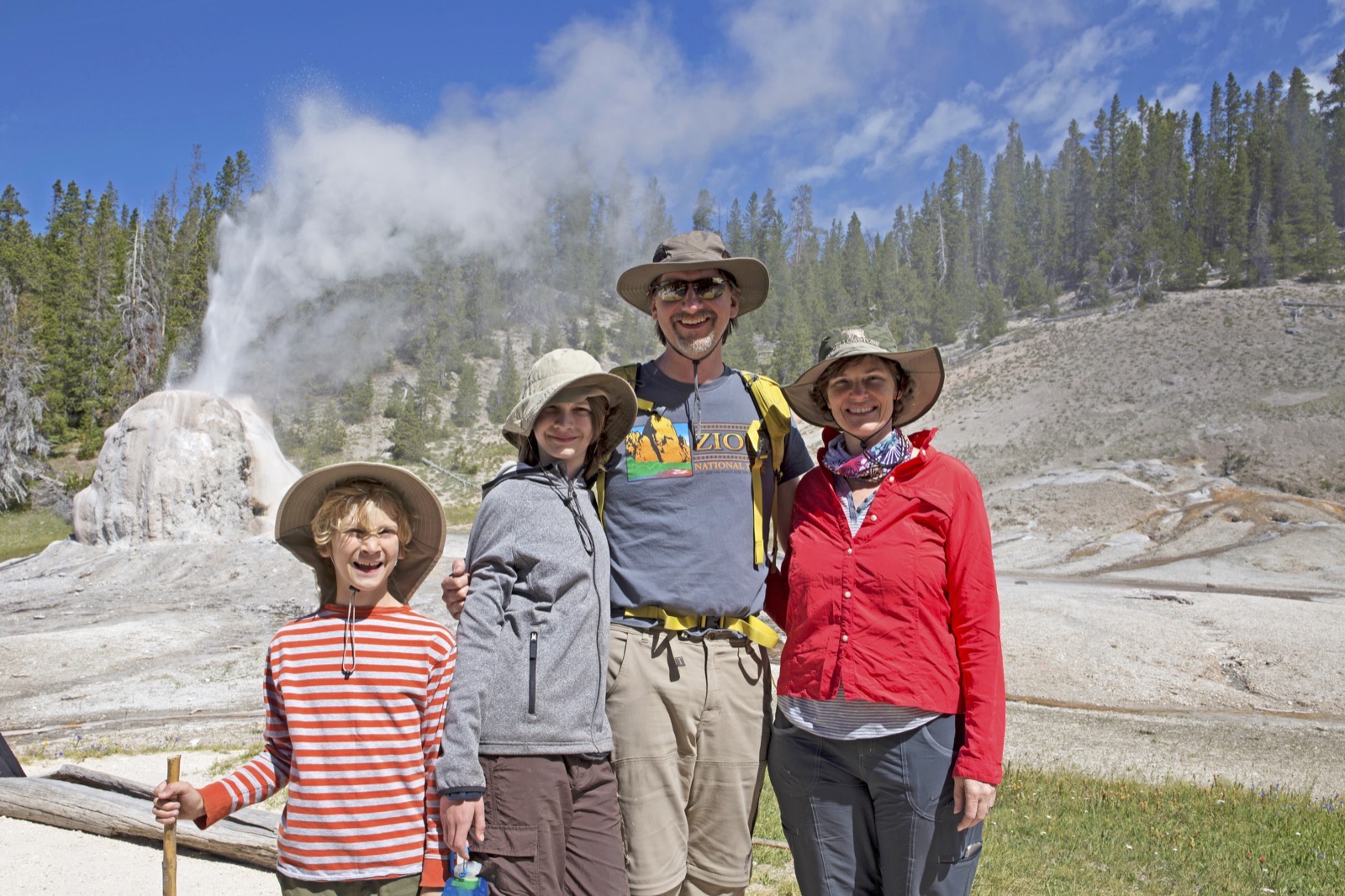 Parents and two kids stand in front of Old Faithful geyser in Yellowstone.